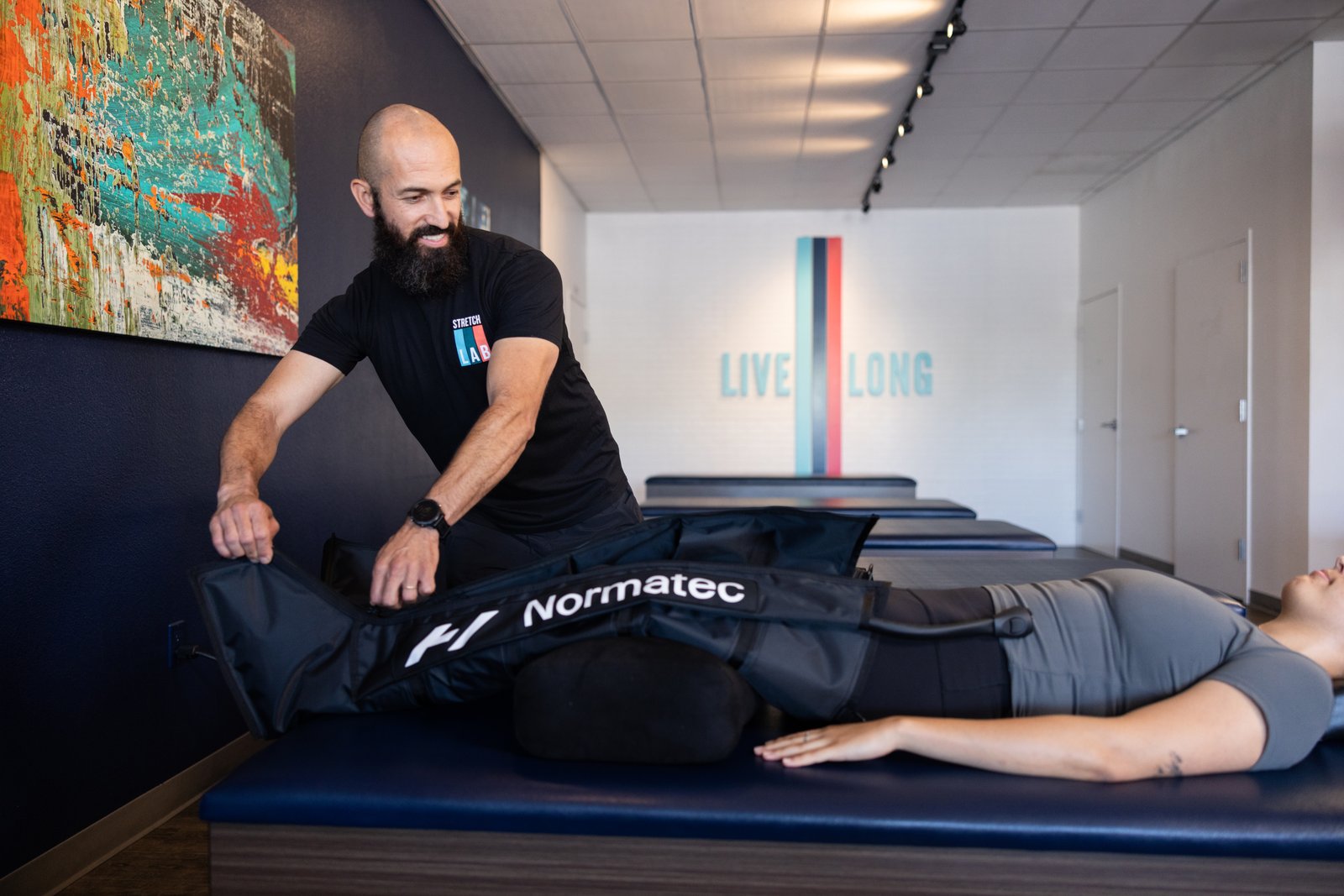 StretchLab trained stretch practitioner using Normatec compression therapy leg attachment on StretchLab member's legs