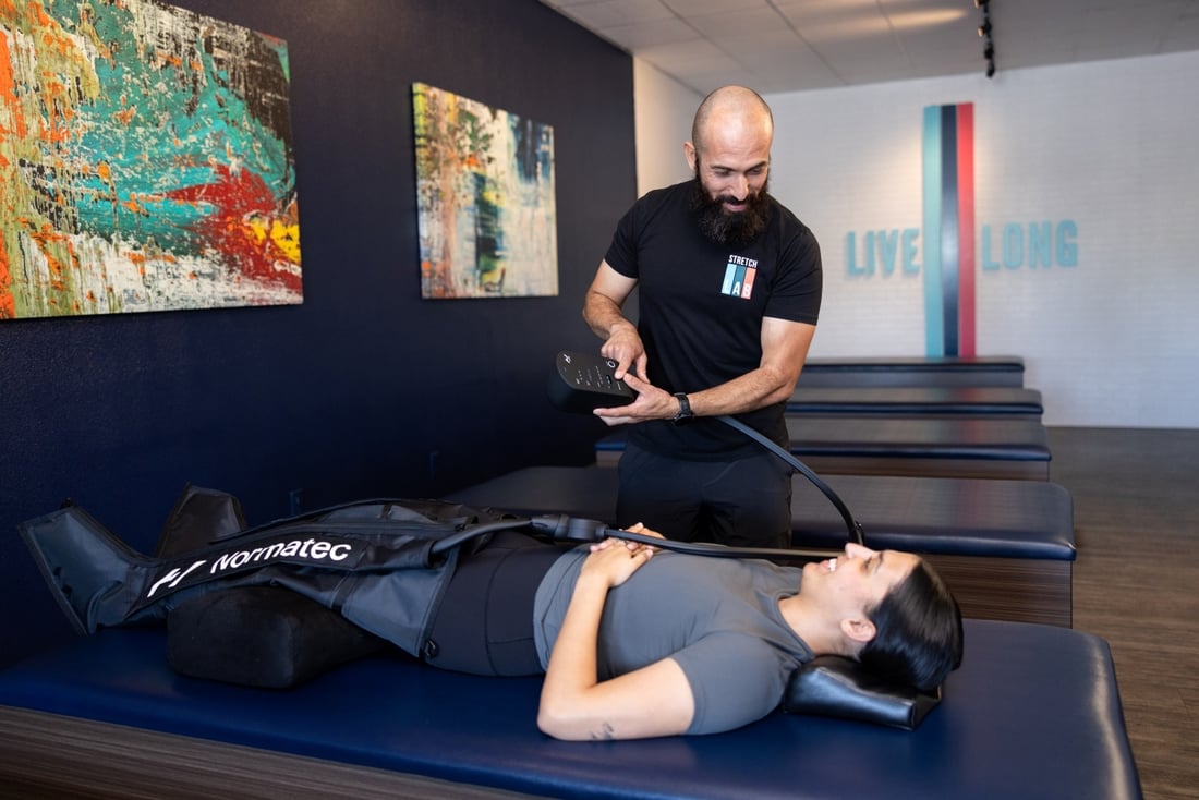 StretchLab stretch practitioner guiding woman through Normatec compression therapy