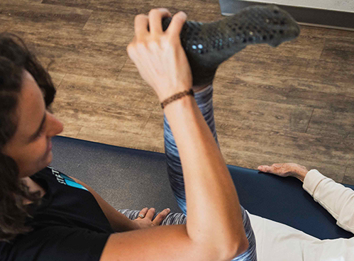 aerial view of 50 year old female guest smiling with comfort and relief, receiving hamstring stretches from an expert flexologist on a padded blue bench at stretchlab studio